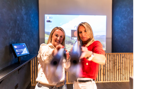 Two women aiming clayshot rifles at the camera
