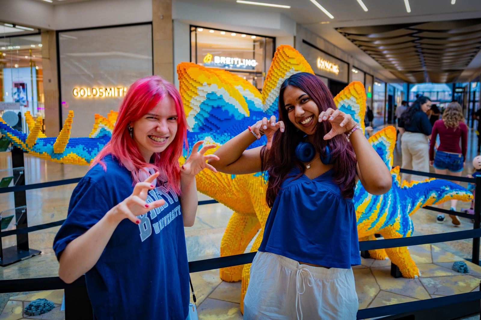 Two teenage girls pretending to be dinosaurs beside Stegosaurus brick model