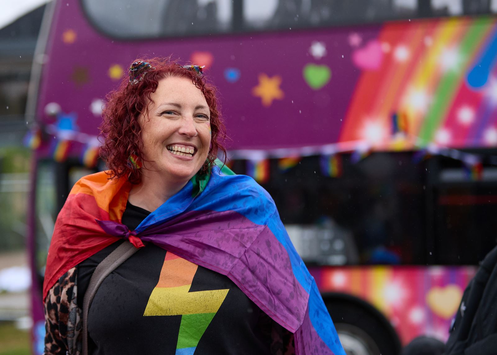 woman dressed in rainbow in front of purple bus